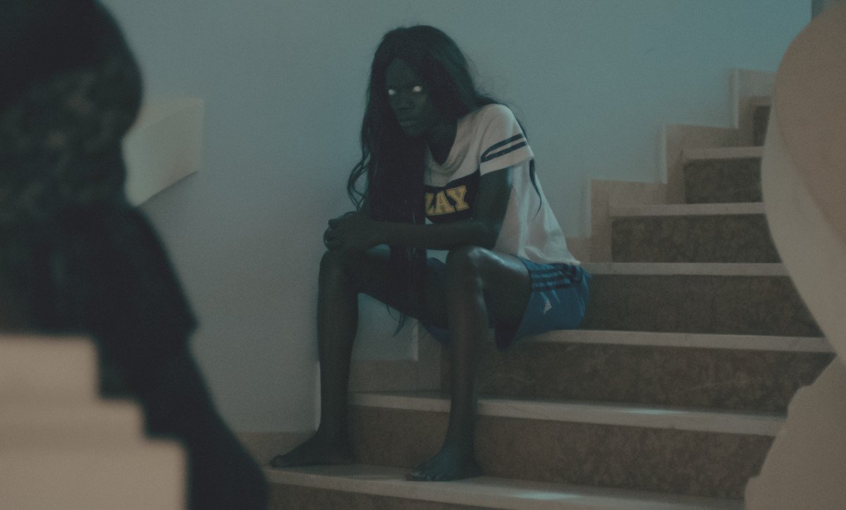 A woman with milky eyes sits upon a staircase.