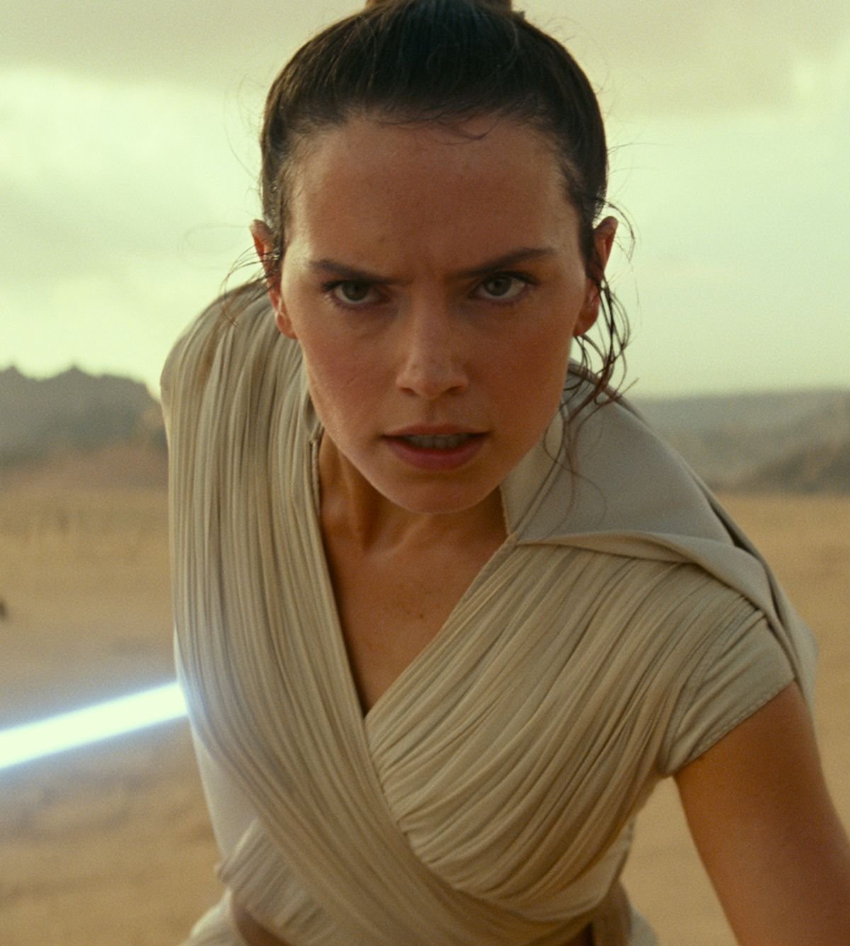 Rey, with lightsaber out, prepares for a fight on a desert planet in Star Wars: The Rise of Skywalker