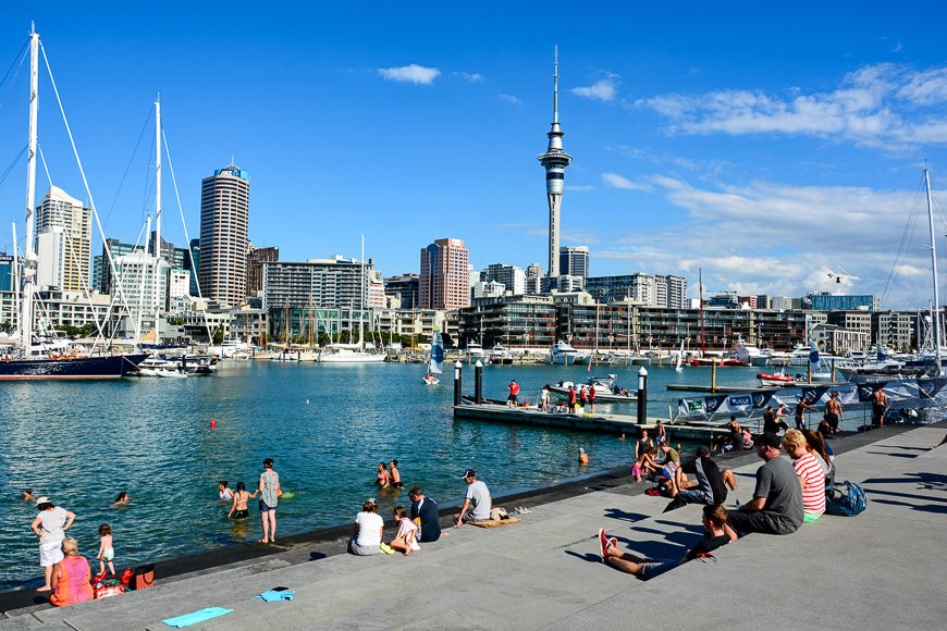 View from the Wynyard Quarter in Auckland, with people, residential and commercial buildings, Sky Tower and boats.