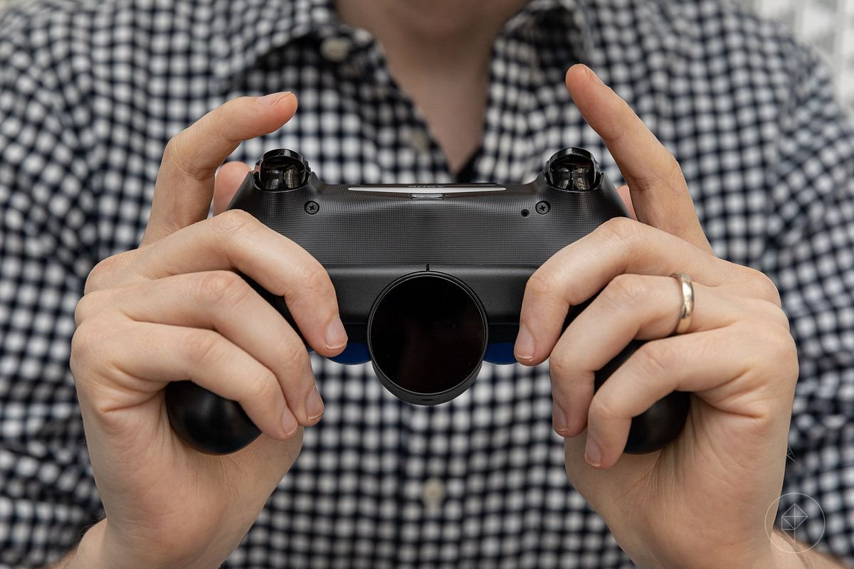 Two hands holding the Sony PS4 controller with the DualShock 4 Back Button Attachment showing the underside