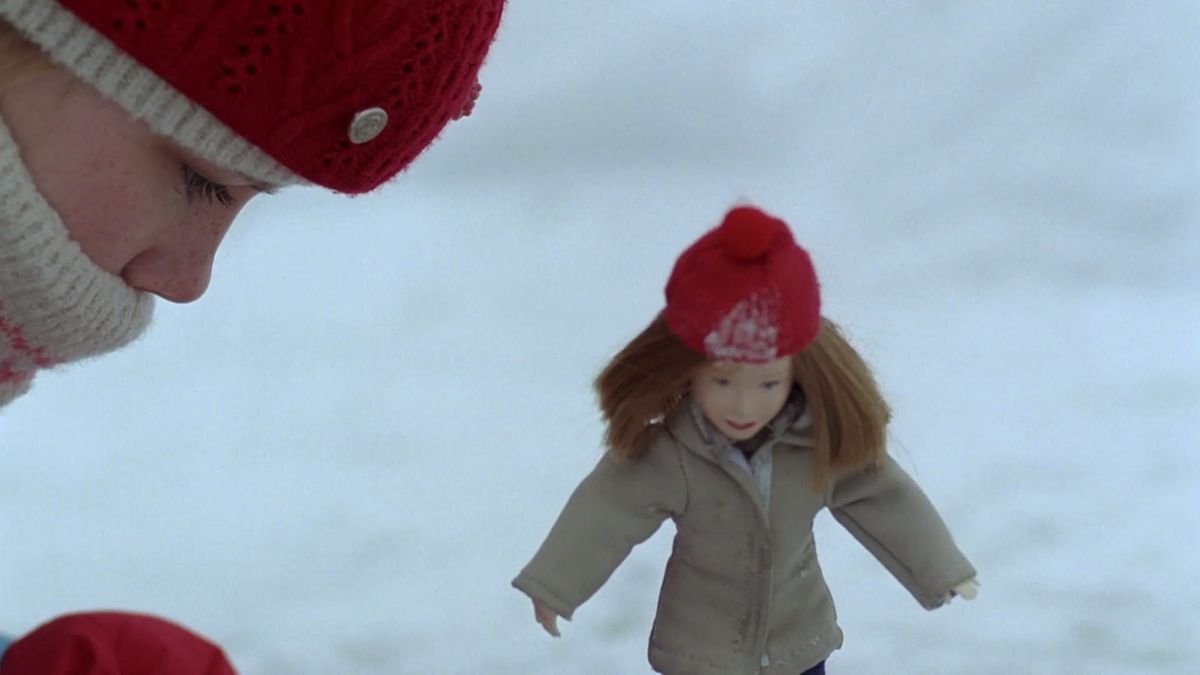 A girl next to a doll in the snow.