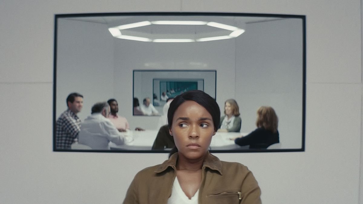 Janelle Monáe sits in a white room in front of a mirror or screen featuring a group of people sitting around a white table in season 2 of Amazon’s Homecoming.