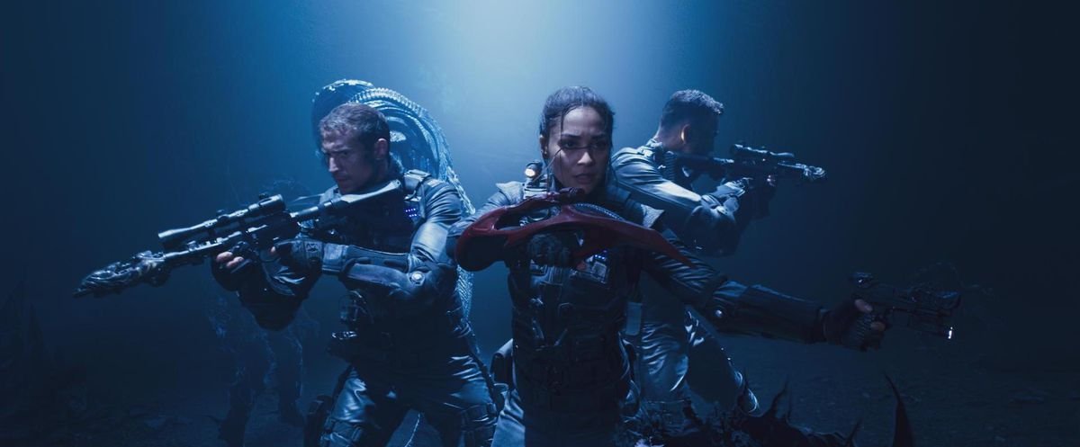 Lindsey Morgan and her co-stars in military gear, under blue light, waving their guns threateningly