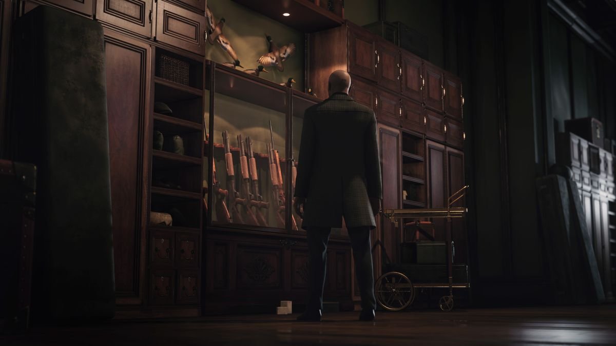 Agent 47 stands in front of a glass case of hunting rifles in Dartmoor in Hitman 3