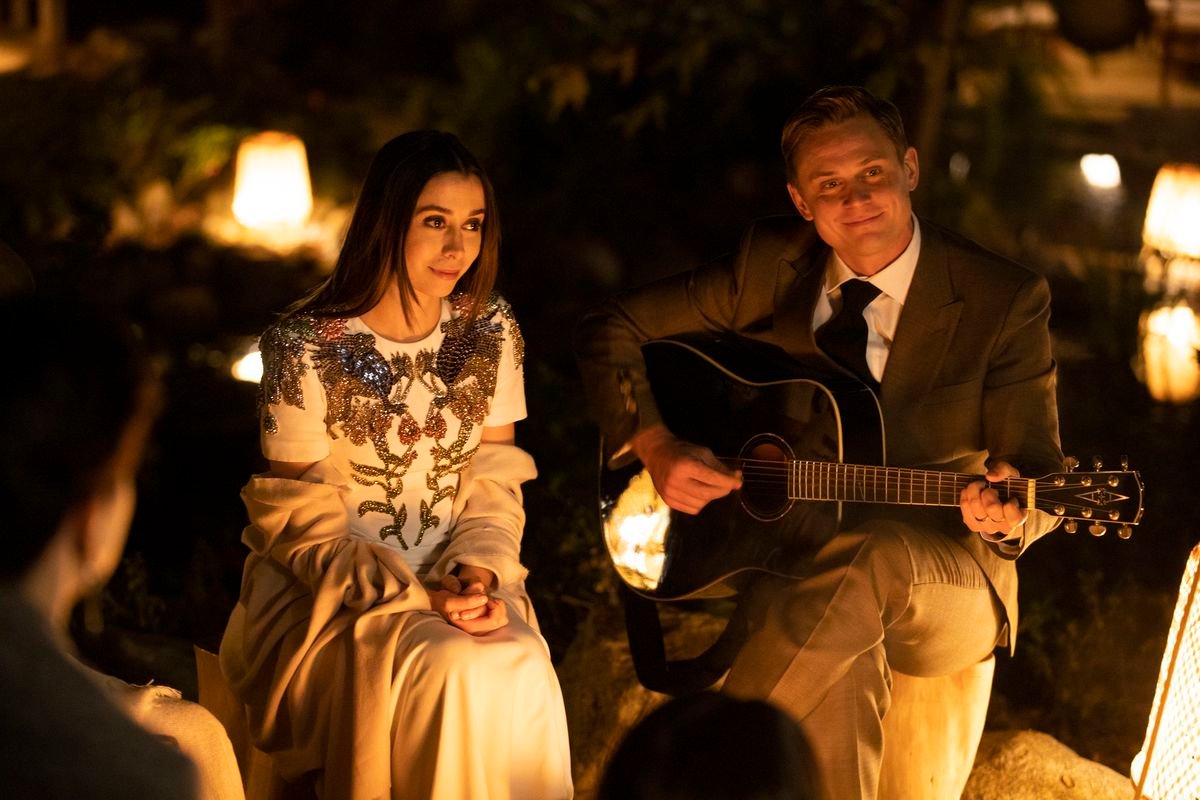 Cristin Milioti and Billy Magnussen sit together at night in a dress and suit, respectively, while Magnussen plays guitar in character as Byron Gogol.