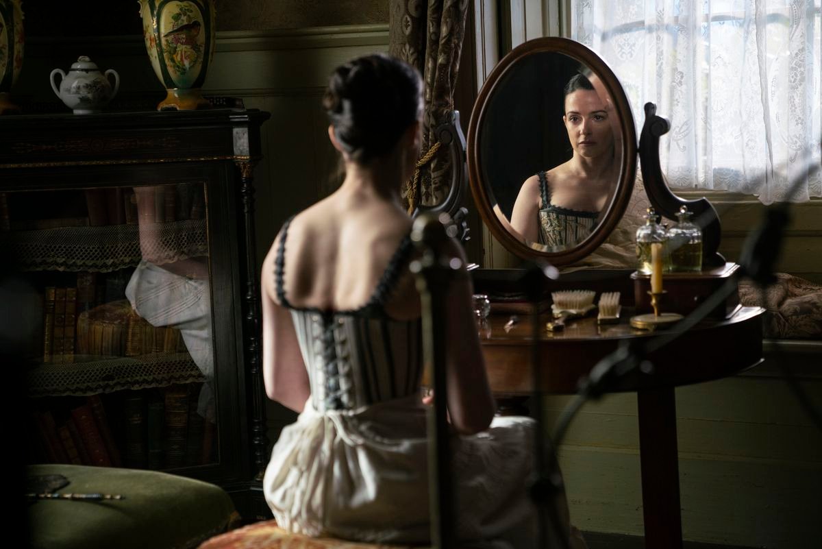 Laura Donnelly, in a corset and underskirt, looks in a mirror in The Nevers