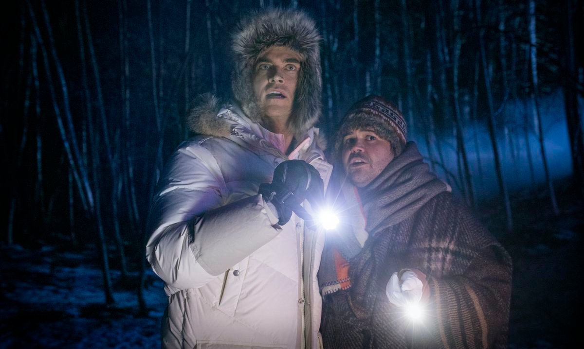 Cheyenne Jackson and Harvey Guillén huddle together outdoors, clutching flashlights, in Werewolves Within