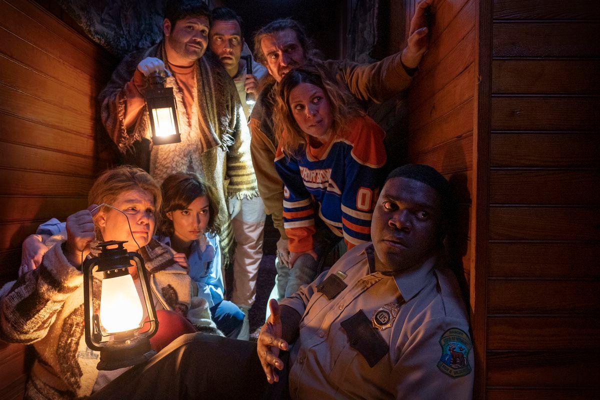 Seven of Werewolves Within’s cast members huddle together nervously, clutching lanterns