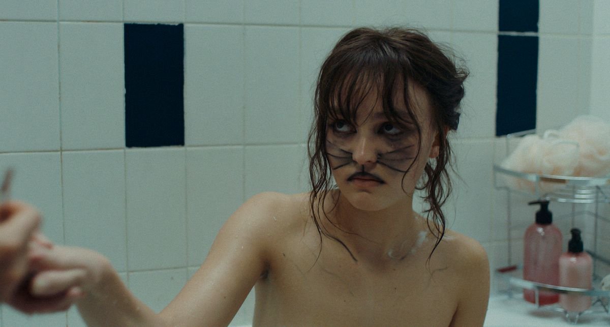 Lily Rose Depp, with cat whiskers painted on her face, looks distrustfully offscreen in Wolf