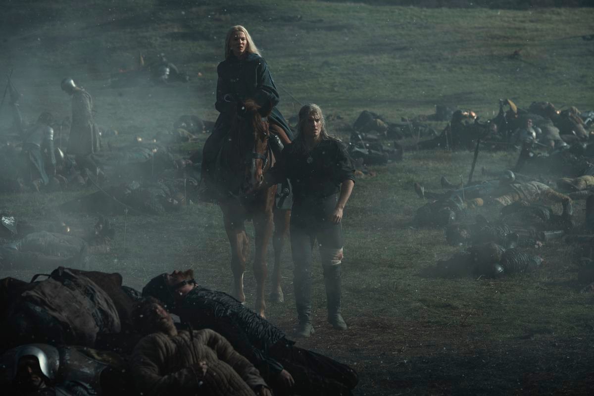 Geralt leads his horse on foot while Ciri rides through a battlefield in Netflix’s The Witcher