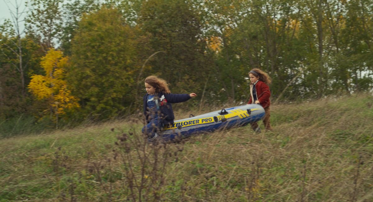 Nelly and her mother, both at the same age, run through the forest with an inflatable raft in Petite Maman