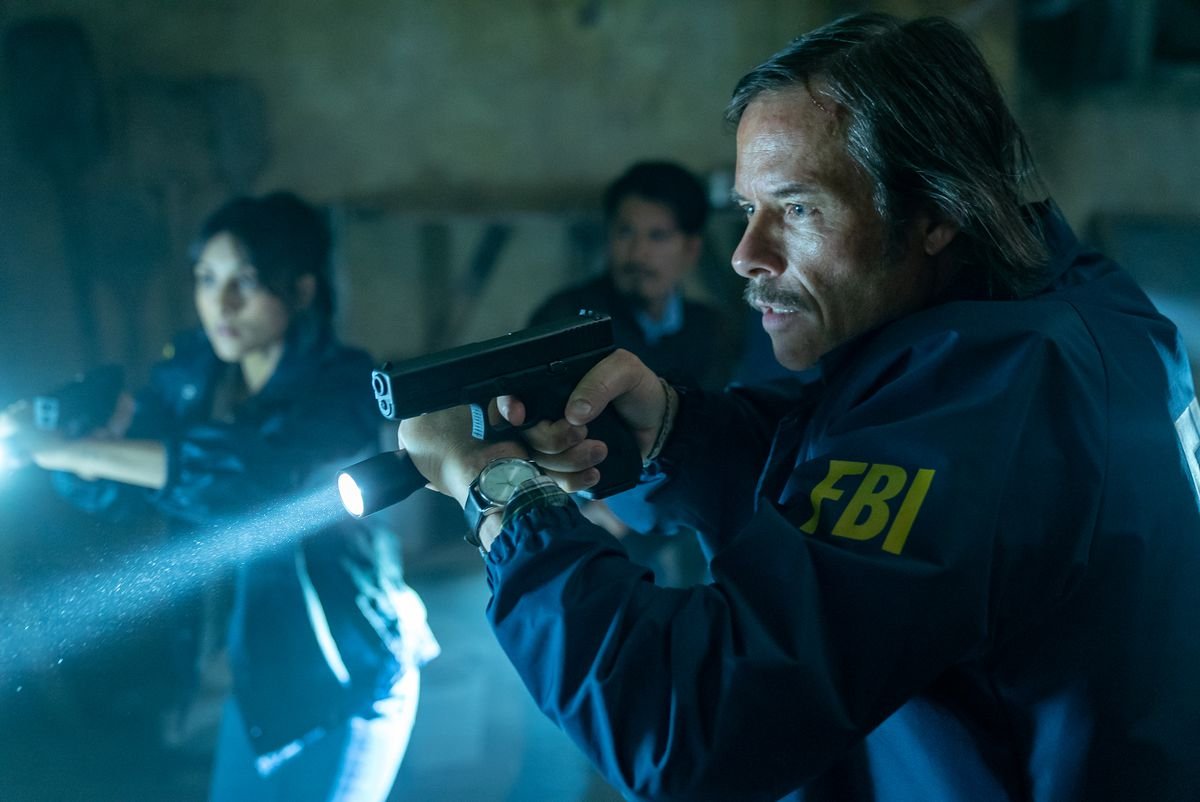 Guy Pearce in an FBI jacket wields a pistol and a flashlight in the film Memory.