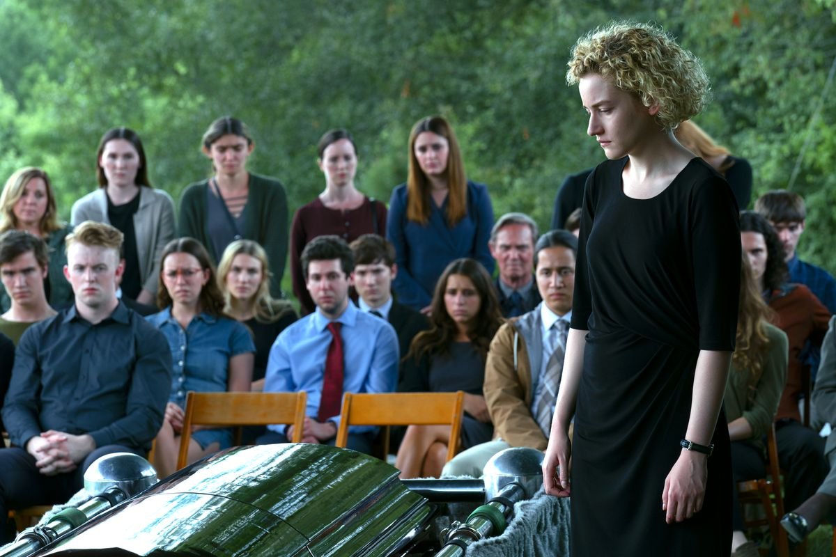 Julia Garner looking down at a coffin at a funeral