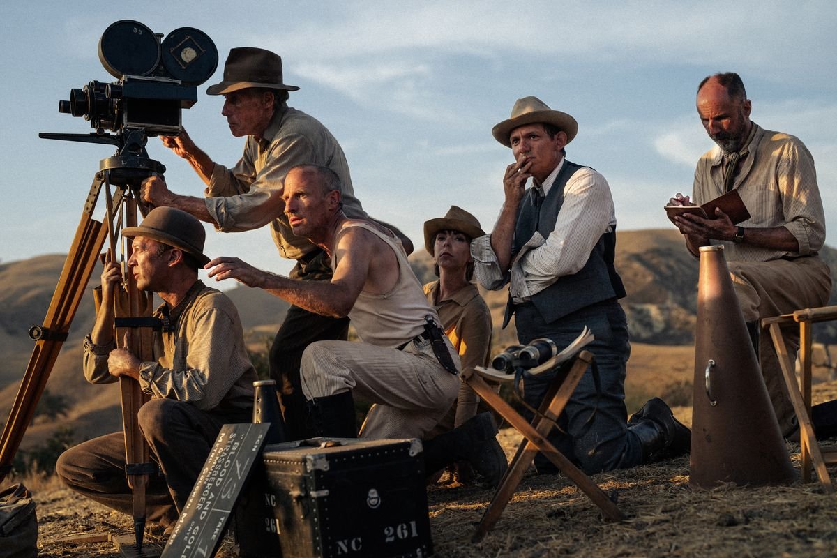 A director and crew gather behind a camera in the 1920s as the sun sets off-screen in front of them in the California desert, in a scene from the film Babylon