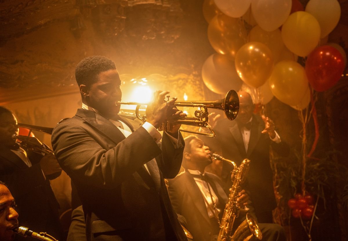 Trumpeter Sidney Palmer plays his horn with his band, all dressed in tuxes against the golden glow and balloons of the debauched party around them in the film Babylon