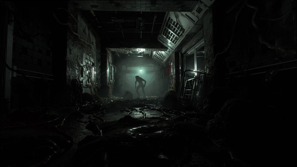 A dark industrial hallway is covered in gore and tentacles, with a mutant in silhouette in the background, in a screenshot from The Callisto Protocol