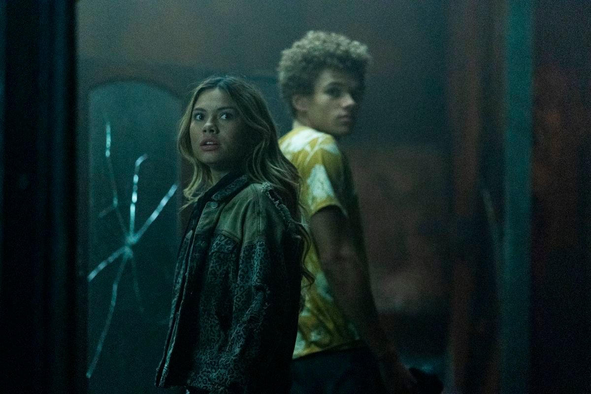 Bella Shepard as Blake Navarro and Armani Jackson as Everett Lang stand back to back in front of a cracked mirror in a dusty old house in The Wolf Pack