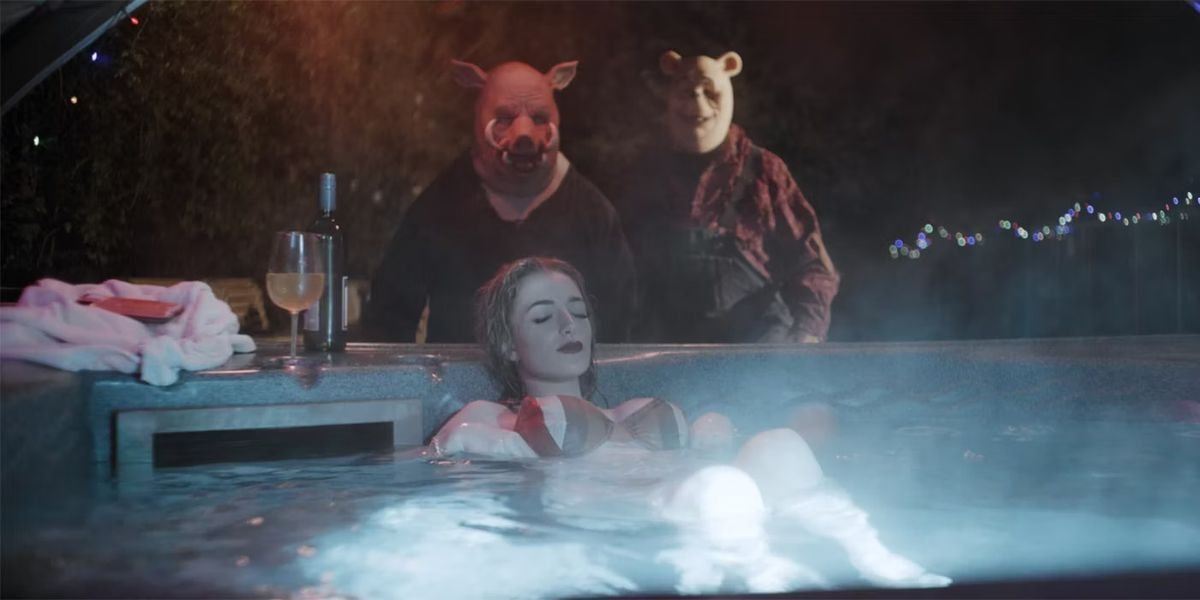 A bikini-clad woman (Natasha Tosini) lounges with her eyes closed in an outdoor hot tub at night while killers Pooh (Craig David Dowsett) and Piglet (Chris Cordell) sneak up behind her in Winnie the Pooh: Blood and Honey