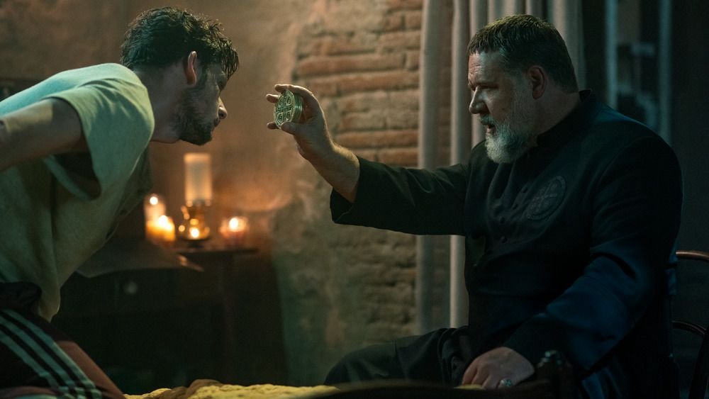 Russell Crowe in the Pope’s Exorcist holding a medallion with the Vatican’s seal on it to a person who is tied to a bed and possibly possessed