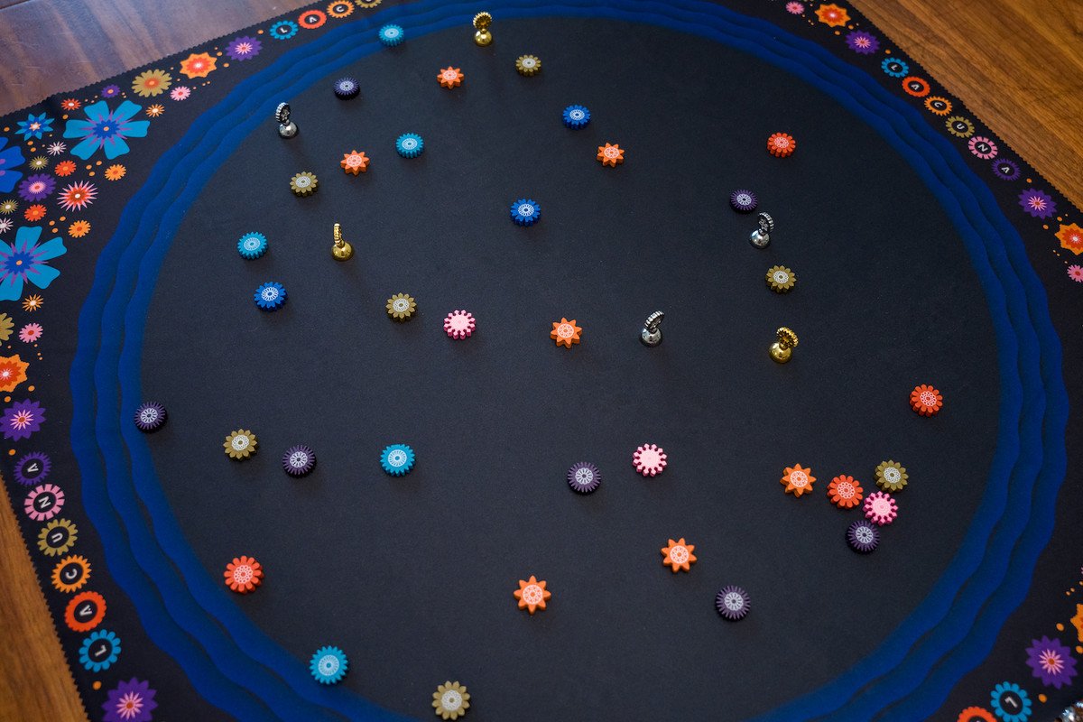 Lacuna laid out to play: Wooden tokens representing flowers on a large, black pond with a blue, wavey edge.