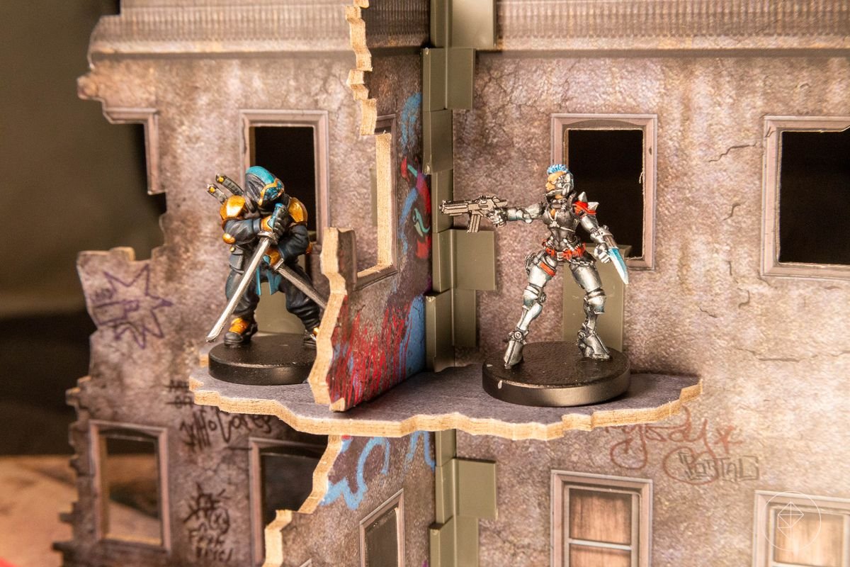 Two figures stand inside a cardboard mockup of a ruined urban building.