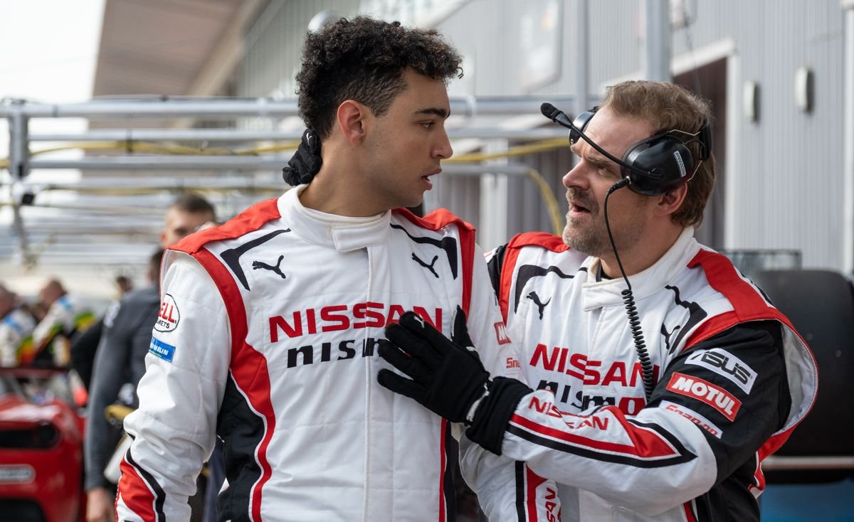 David Harbour’s race engineer Jack Salter reassures racing driver Jann Mardenboroguh (Archie Madekwe), both wearing Nissan racing suits, in Gran Turismo