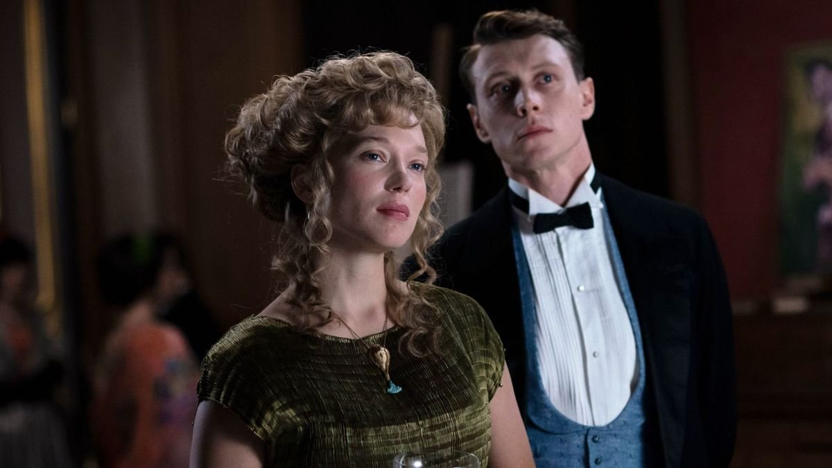 Gabrielle (Léa Seydoux) and Louis (George MacKay), a pale man and woman dressed in 1910 Parisian fashions — her in a green gown with her hair in ringlets, him in a black bow tie and jacket and blue vest — stand together, looking offscreen in a disaffected way in The Beast