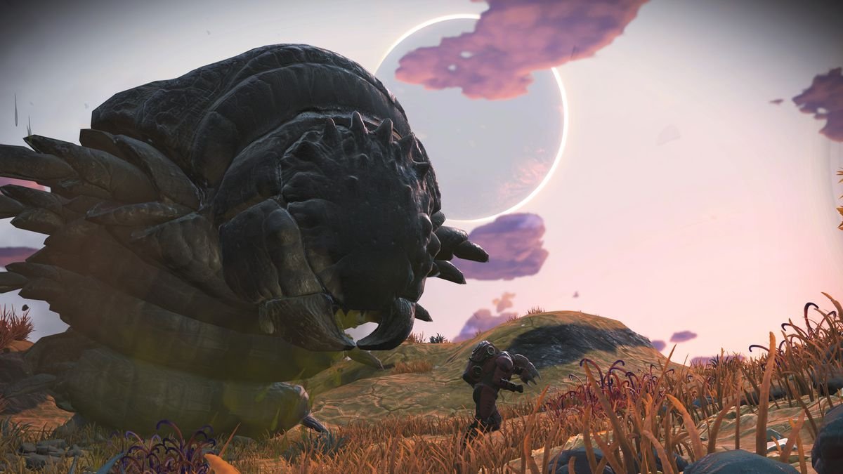 A massive, gray-green alien follows behind a humanoid explorer on a planet with yellow grass and purple clouds in No Man’s Sky