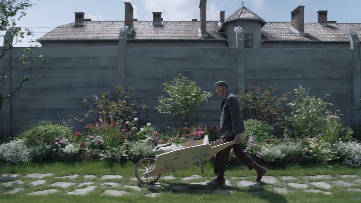 A gardener pushes a wheelbarrow along a garden wall near Auschwitz in The Zone of Interest 