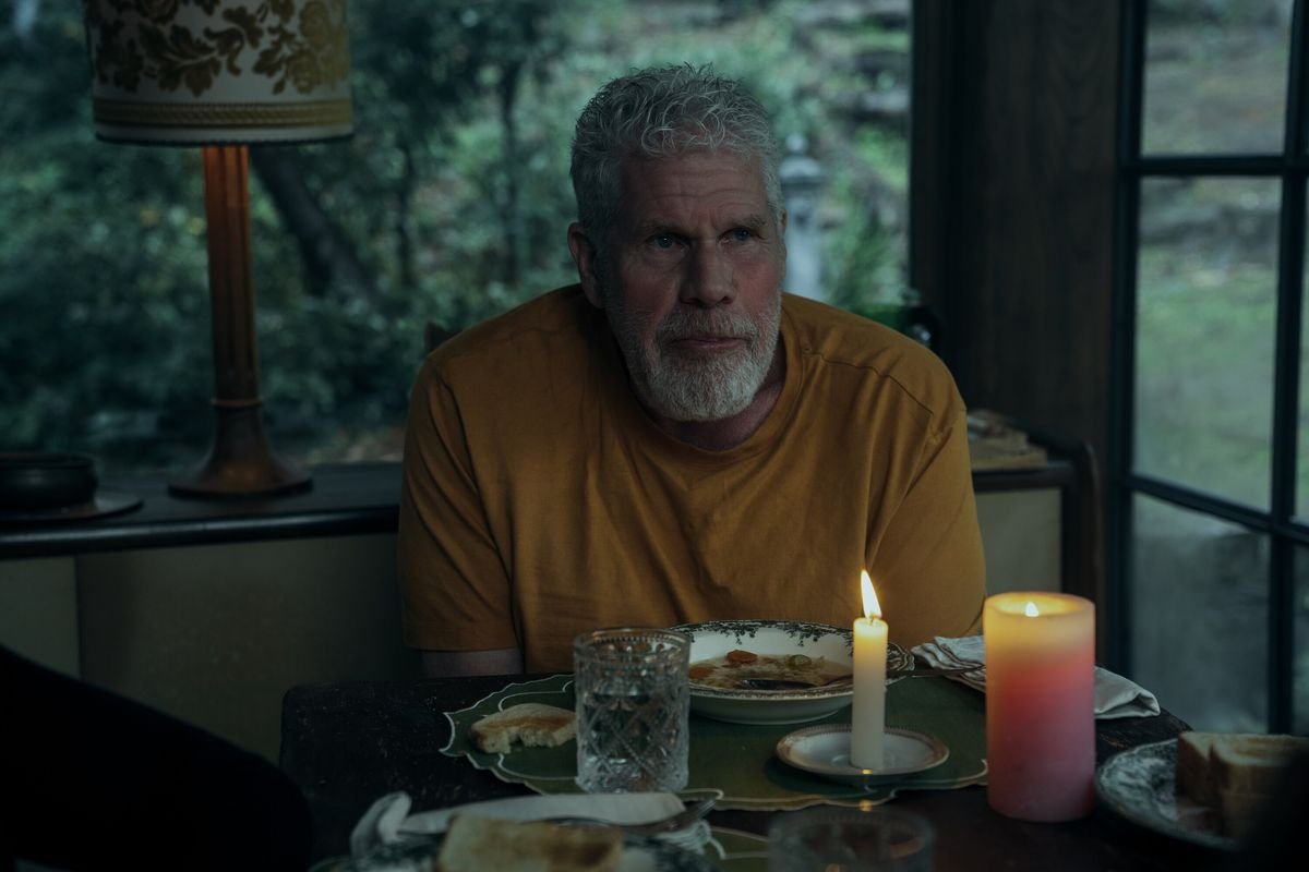 Ron Perlman looks sad in a yellow T-shirt at a candlelit dinner table at twilight in Mr. & Mrs. Smith