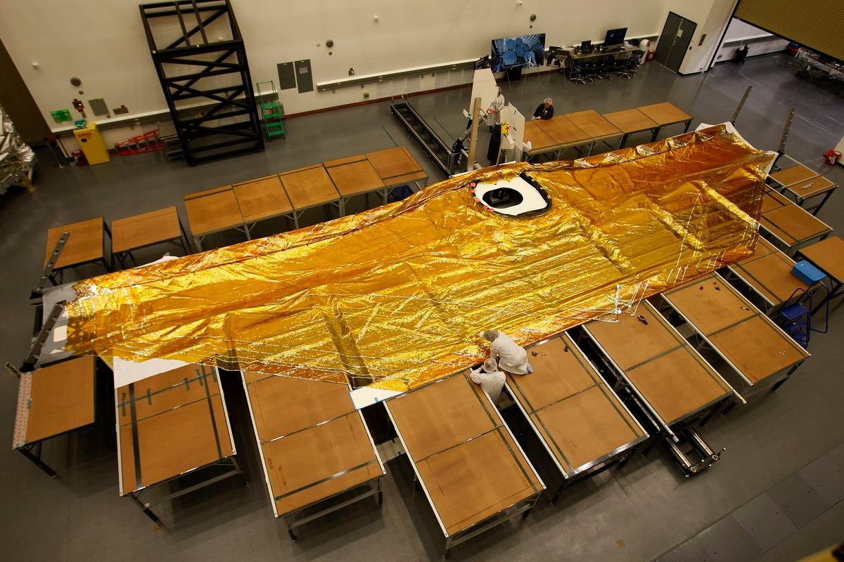 A gold five-layer sun shield stretched across a piece of the James Webb Space Telescope which is laid out on the floor
