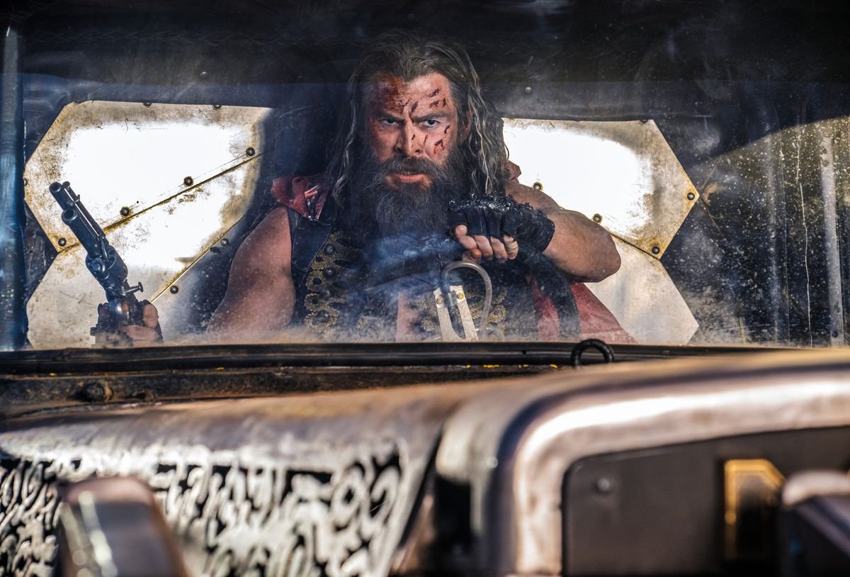 Dementus (Chris Hemsworth), a shaggy-haired, shaggy-bearded Wasteland warrior, holds a gun in one hand and steers a vehicle with the other in George Miller’s Furiosa