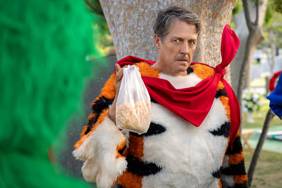 Hugh Grant wears a mustache and a Tony the Tiger costume with the mask off in the Netflix movie Unfrosted.