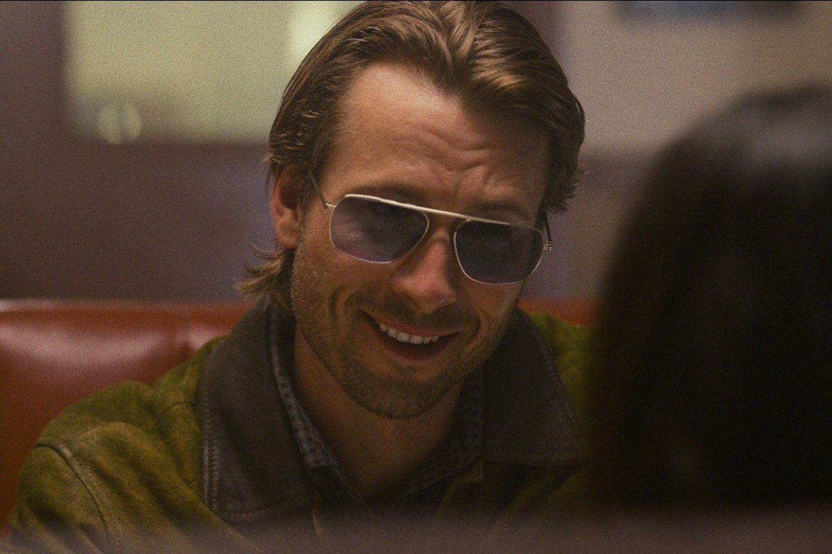 Glen Powell grinning suavely in shades in Hit Man
