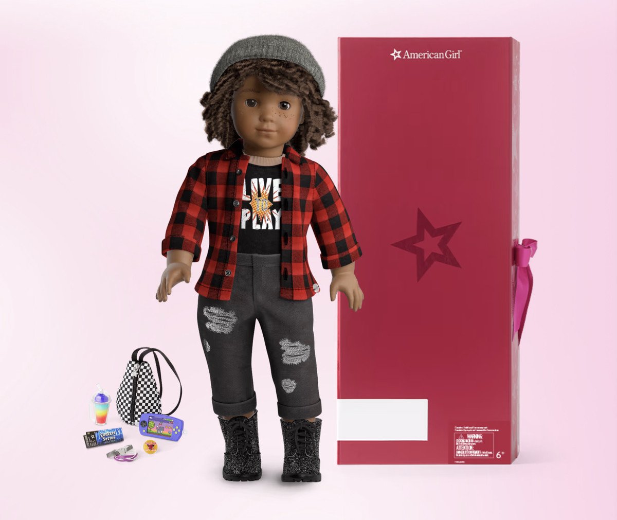 A create-your-own American Girl doll is shown wearing a flannel and ripped jeans. The doll has short, curly brown hair, brown skin, and freckles.